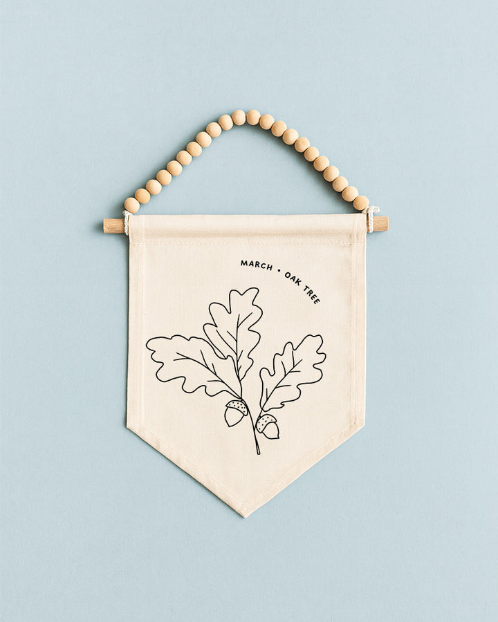 A beige banner with a black line drawing of an oak tree and acorns, hanging on a light blue background.