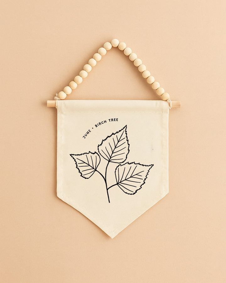 A beaded banner with a simple black and white illustration of three leaves hanging on a peach-colored wall.
