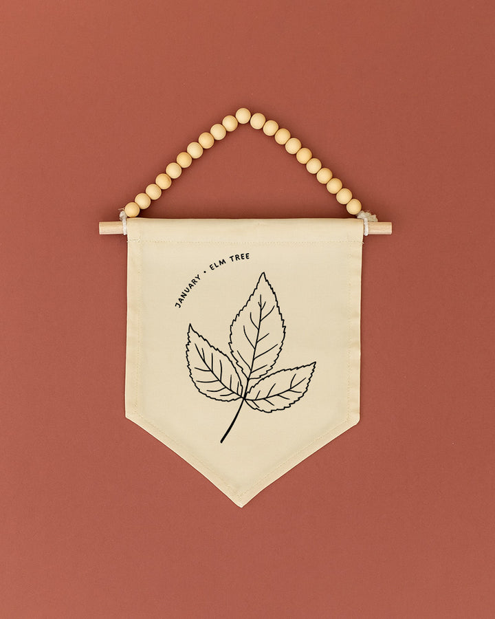 A beaded banner with a simple black and white leaf design hangs against a red background.