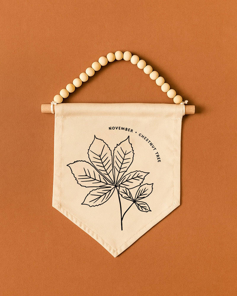 A banner with a leaf design and the text "November | Chestnut Tree" hanging on a wooden bead.