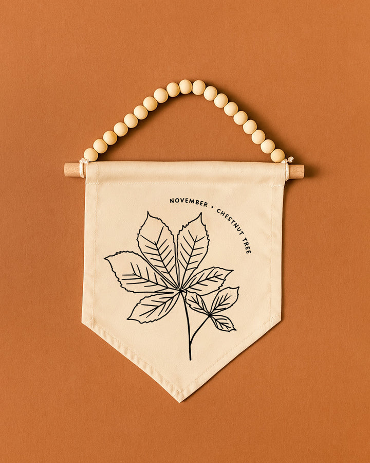 A banner with a leaf design and the text "November | Chestnut Tree" hanging on a wooden bead.