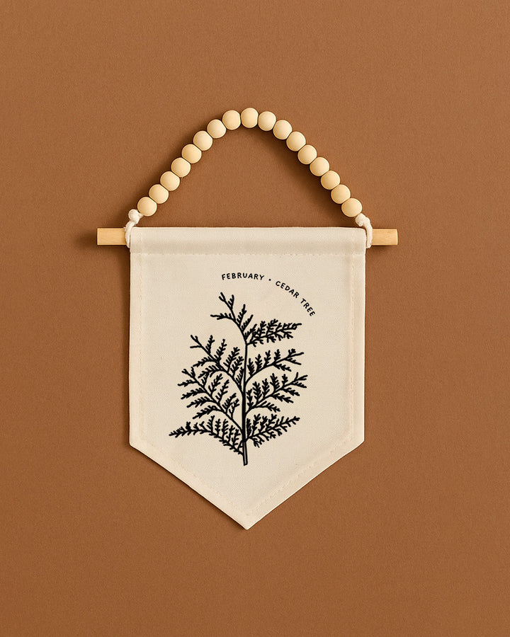 A beaded banner with a black and white illustration of a tree hangs on a brown wall.