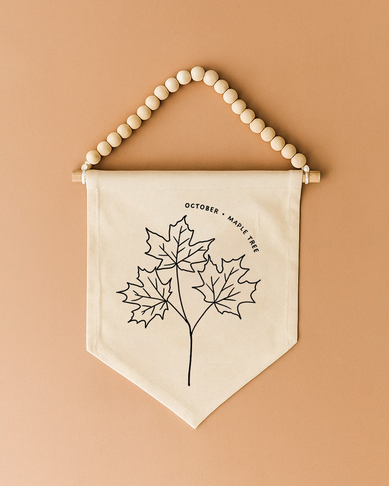 A beaded banner with a black and white illustration of three maple leaves hanging on a wall.