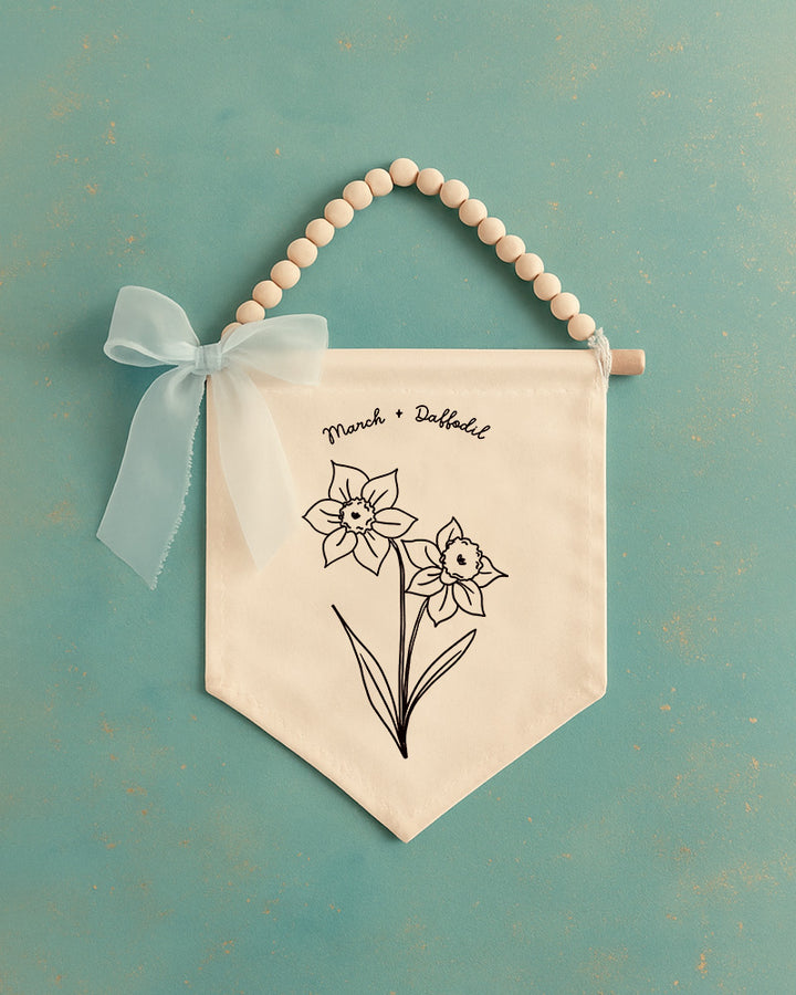 A banner with a floral design hangs against a teal background, accompanied by a white ribbon bow.