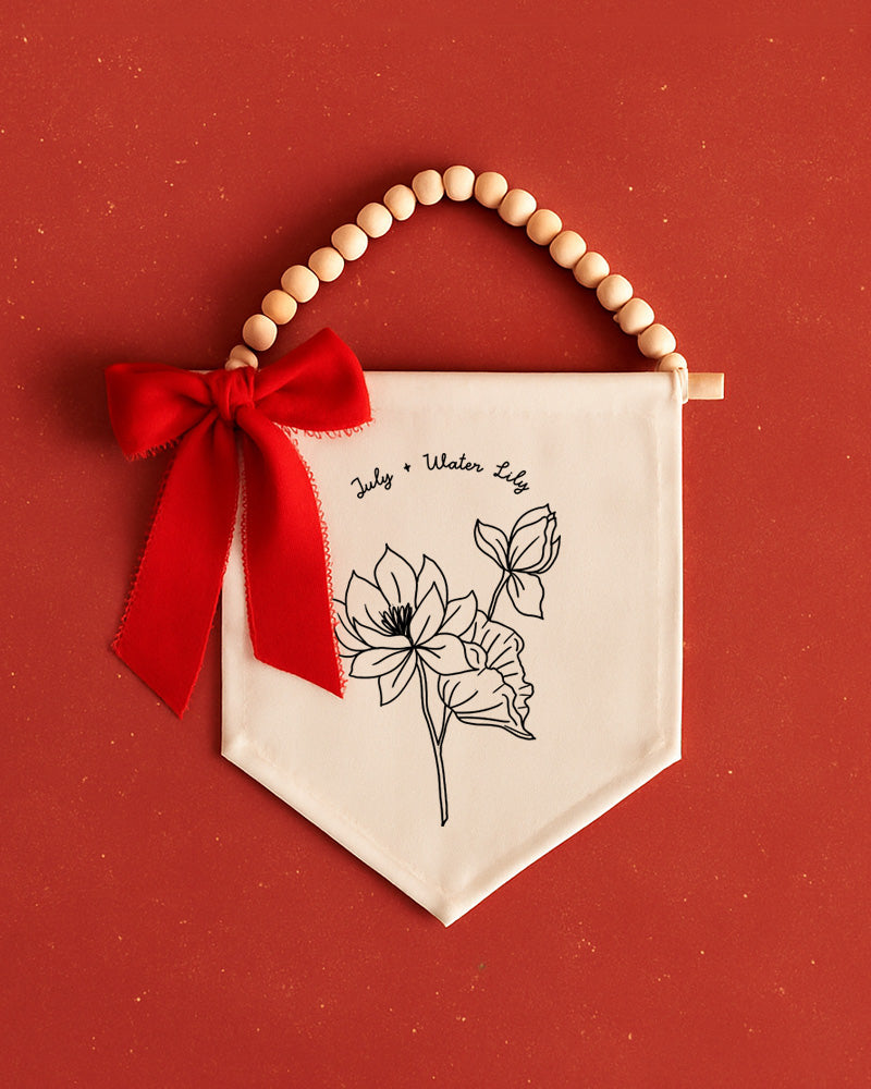 a white banner with a red ribbon and a wooden bead decoration, set against a red background.