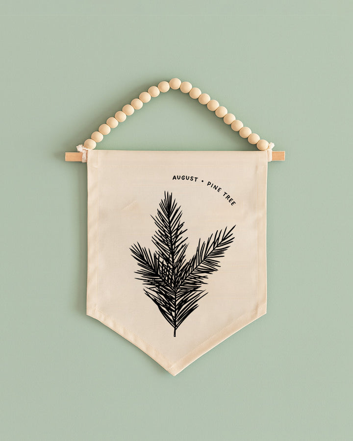 A beaded banner with a black pine tree design hangs against a light green background.