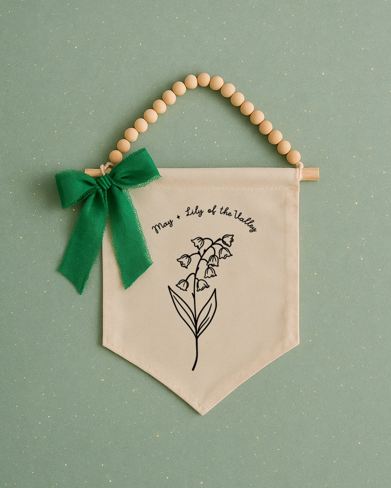 A banner with a lily of the valley design and a green ribbon bow is displayed against a green background.