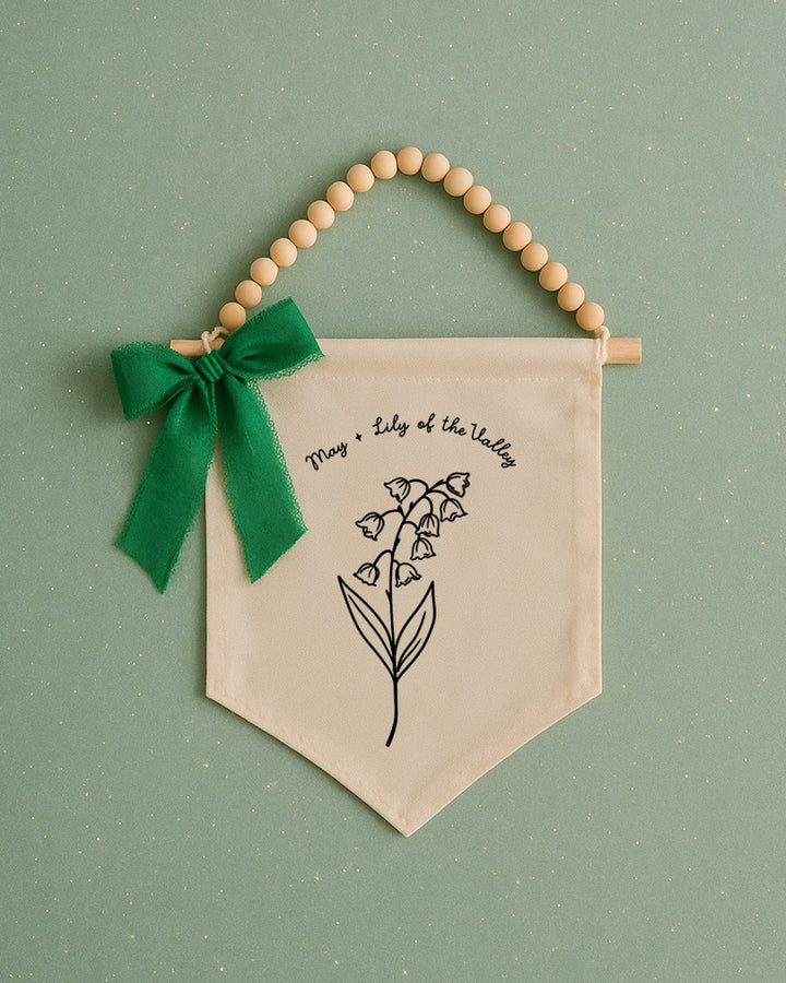 A banner with a lily of the valley design and a green ribbon bow is displayed against a green background.