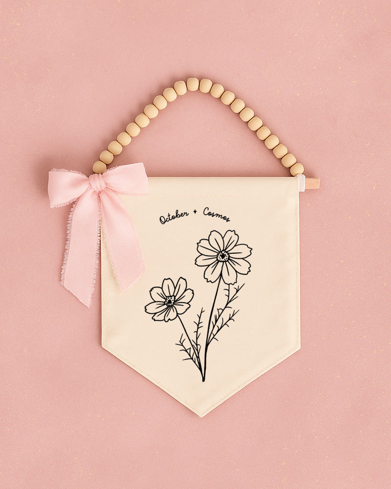 A banner with a floral design and a bow is hanging on a pink background.