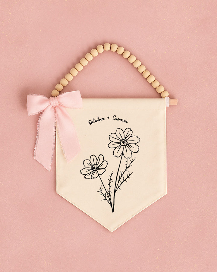 A banner with a floral design and a bow is hanging on a pink background.