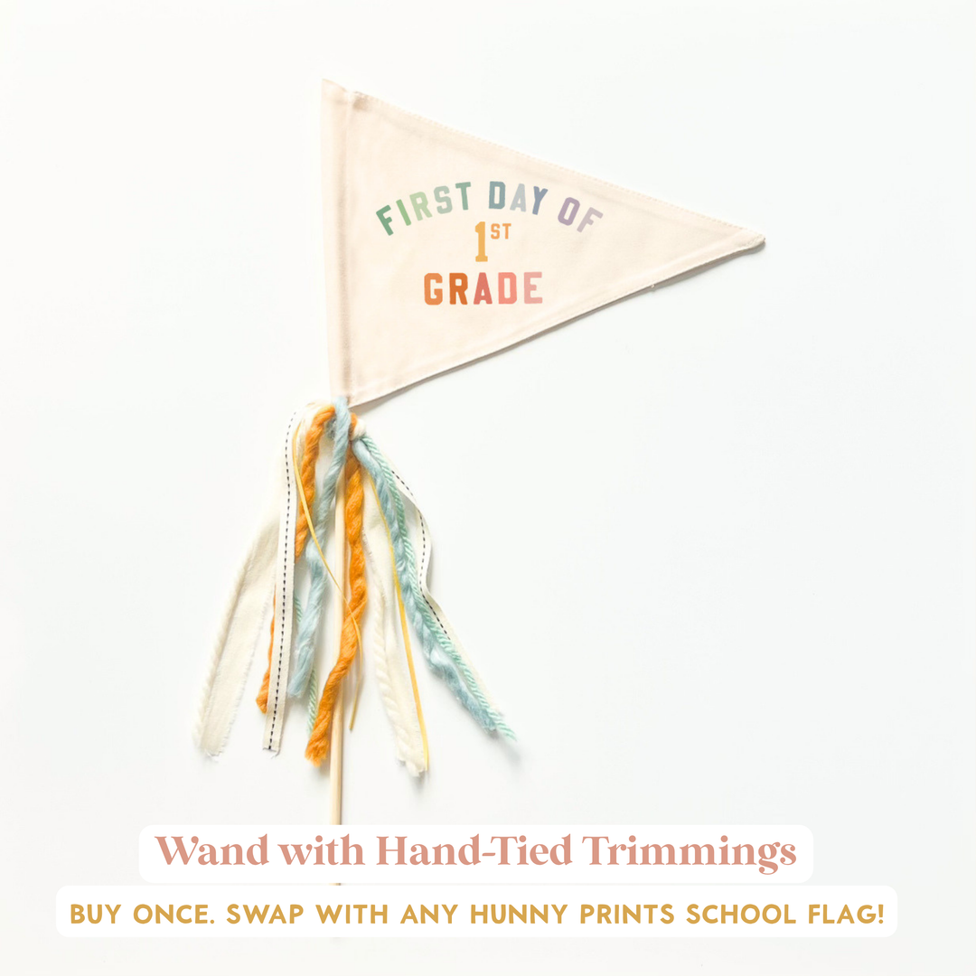 a hand-tied trimming on a white background, with a triangular flag attached to it that says "FIRST DAY OF 1ST GRADE".