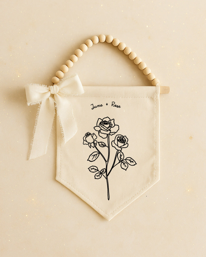 A banner with a floral design and a ribbon bow, hanging on a beige background.